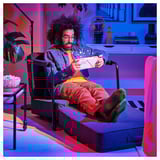 Homem em roupas coloridas lê, descansando em poltrona/cadeira transformável com almofada de assento dobrada.