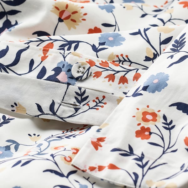 Edredão floral conjunto close-up; creme com estampas florais azul marinho e vermelho, com cantos abotoados. Algodão orgânico macio e respirável.