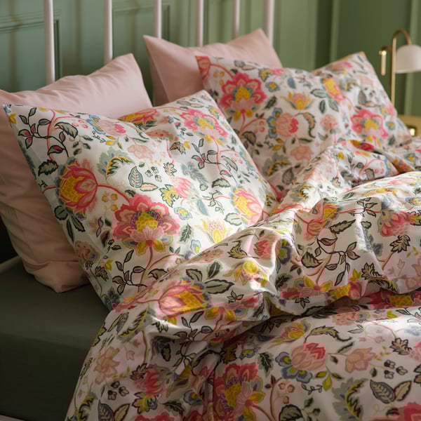 Cama com capa de edredão e almofadas coloridas com estampa floral, contra paredes verdes, exibindo padrões vibrantes e textura de tecido suave.