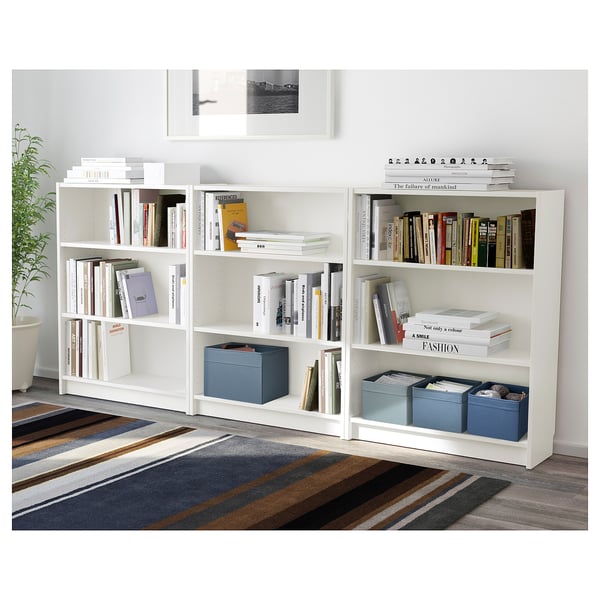 Estante branca com livros, várias caixas de tecido em azul, ambiente de quarto elegante, serve como solução de armazenamento.