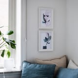Duas obras de arte coloridas emolduradas penduradas acima de um sofá azul, com desenhos abstratos em roxos e azuis.