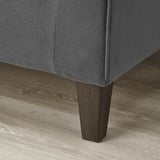 Close-up do sofá: estofamento cinza escuro, pernas cônicas de madeira, piso polido.