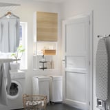 Lavandaria moderna com armários ENHET brancos, detalhes em madeira, armário espelhado e prateleiras de arrumação. Pisos escuros, paredes brancas.