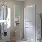 Lavandaria moderna com módulo de arrumação ENHET verde claro, toalhas, material de limpeza, máquina de lavar roupa, roupa dobrada e cesto de roupa suja.