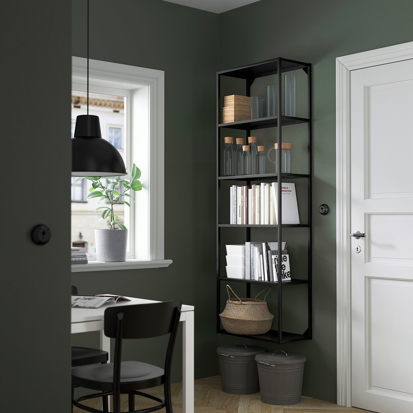 Home office moderno com prateleira preta ENHET, com livros e vasos. Ao lado de uma mesa branca com cadeira, planta e porta branca.