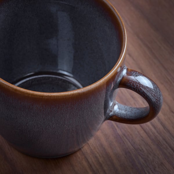 Caneca artesanal com acabamento rústico, brilhante sobre mesa de madeira.