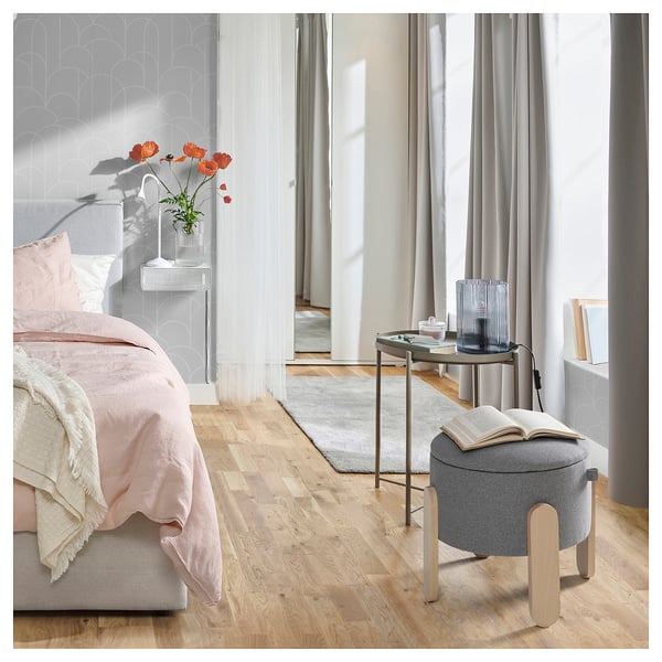 Quarto moderno com roupa de cama rosa, piso de madeira, pouffe cinza FÖRLUNDA ou mesa lateral, cortinas e papel de parede.