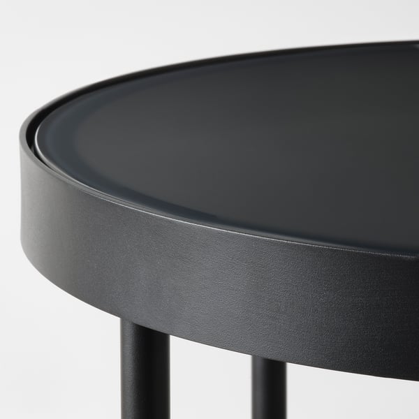 Mesa lateral moderna em preto com tampo de vidro redondo e elegante e pernas de metal resistentes, exalando estilo contemporâneo.