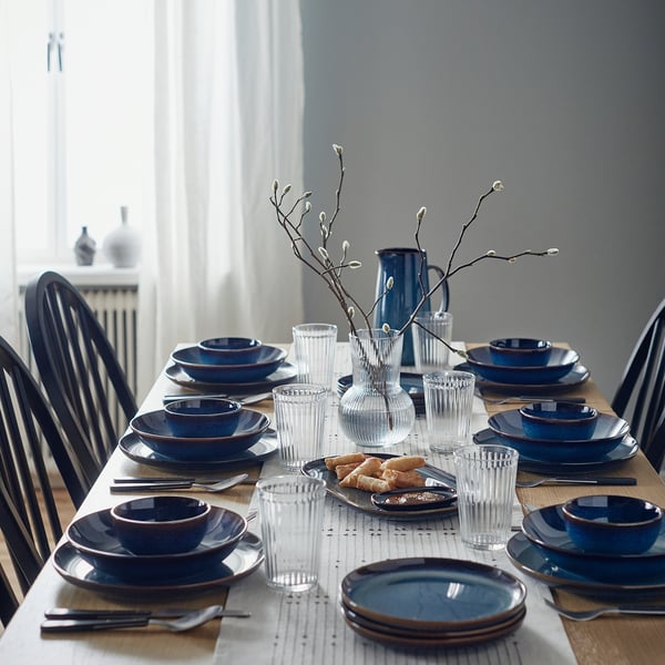 Mesa de grés azul com pratos, copos, talheres e galhos decorativos.