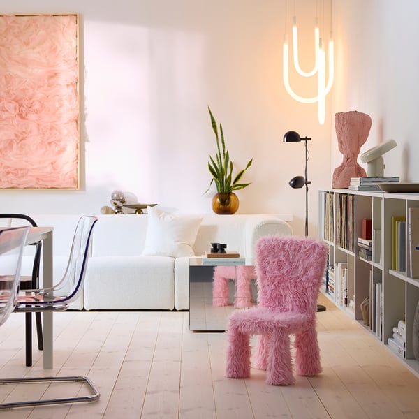 Sala de estar moderna com sofá branco, cadeira peluda rosa, estante e luz de cacto.