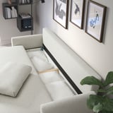 GRUNNARP Sofá-cama com almofadas para fora, mostrando áreas de estar e dormir. Obras de arte e prateleiras ao fundo.