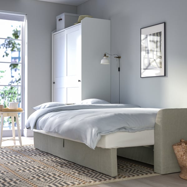 Quarto azul com cama branca, tapete cinza, planta e cesta.