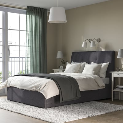 Quarto moderno com cama otomana IDANÄS, roupa de cama branca, mesinhas de cabeceira, luminárias, relógio e paredes verdes.