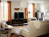 Sala de estar aconchegante com móvel de TV IDANÄS em marrom, sofás macios, cortinas aconchegantes e decoração moderna.