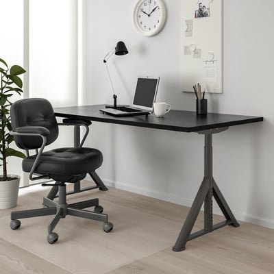 IDÅSEN configuração de mesa e cadeira com rede de cabos, laptop, caneca e lâmpada. Quadro branco e relógio em segundo plano.