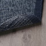 Capacho de algodão azul escuro com manchas brancas, dobrado sobre piso de madeira clara.