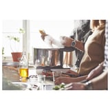 Pessoas cozinhando com uma panela de aço inoxidável IKEA 365+ em um fogão. Eles estão usando vários utensílios e ingredientes de cozinha.