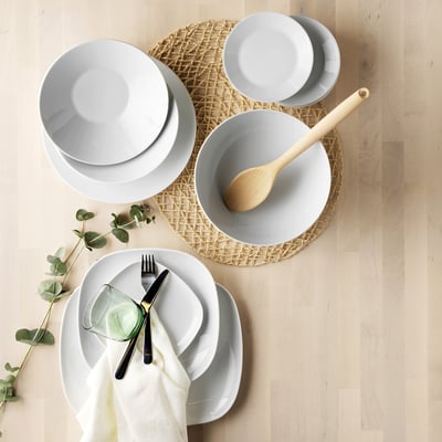 Conjunto de pratos IKEA 365+ branco, porcelana simples e durável, circular, empilhado ordenadamente, com talheres e vegetação.