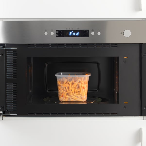 Microondas de aço inoxidável com display digital aquece recipiente de plástico com sobras.