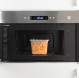 Microondas de aço inoxidável com display digital aquece recipiente de plástico com sobras.