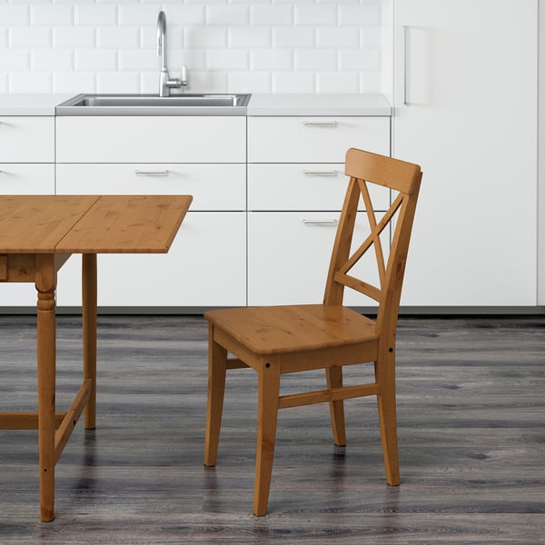 Cadeira de cozinha de madeira com encosto alto, projetada para conforto e durabilidade, posicionada perto de uma mesa correspondente.