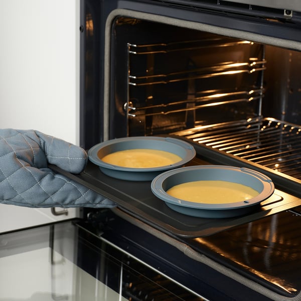 Pessoa colocando formas de cozimento com massa em um forno, usando luvas de forno.