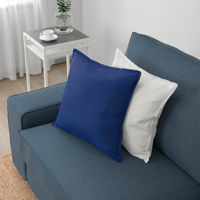 Um sofá azul aconchegante com um travesseiro azul e branco. O sofá foi projetado para conforto e relaxamento com molas ensacadas e espuma.