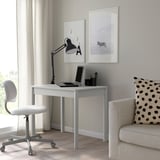 Mesa branca com laptop, artigos de papelaria e decoração.