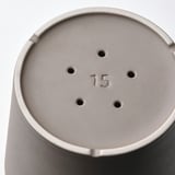 Close-up de uma base de vasos de plantas cinza, rotulada 15. Mostra furos de drenagem, superfície lisa e construção robusta.