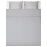 A imagem mostra uma cama cinza bem feita com um conjunto de roupa de cama cinza liso e sedoso, incluindo capa de edredom e duas fronhas, retratando um design minimalista moderno.