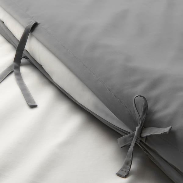 Capa de colcha cinza dobrada com laços de fita, mostrando tecido liso e acabamento decorativo.