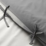 Capa de colcha cinza dobrada com laços de fita, mostrando tecido liso e acabamento decorativo.