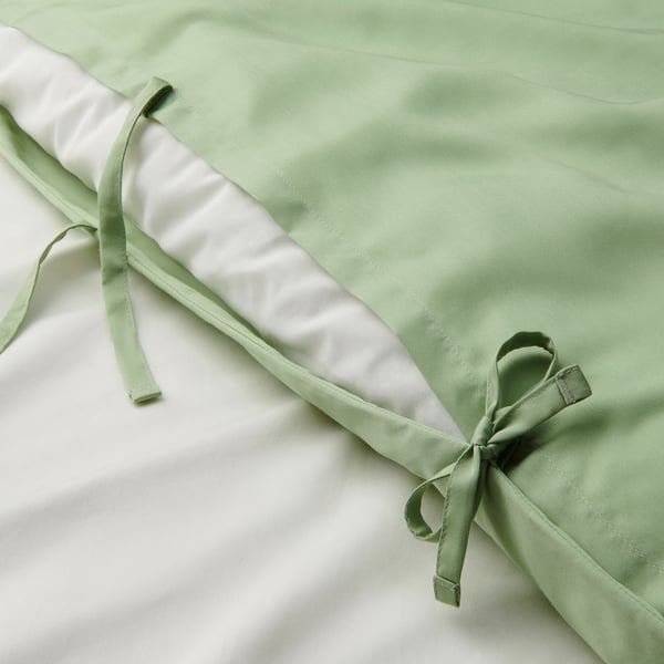 Capa de colcha verde tipo seda com laços e bolso, mostrada parcialmente enrolada.