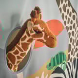 Um brinquedo de girafa de pelúcia espreita através de uma janela circular azul em uma cortina de cama infantil, cercado por estampas vibrantes de safári.