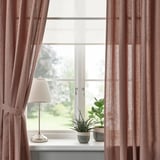 Janela com cortinas marrom-vermelhas, amarradas para trás à vista da vitrine. Abajur à esquerda, plantas à direita.