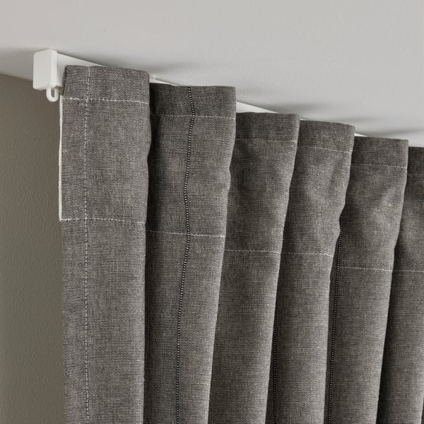 Cortinas cinza com fita de cabeçalho pendem perfeitamente de uma haste de cortina branca, permitindo luz e oferecendo privacidade.