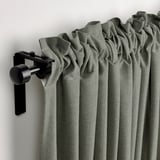 Varão de cortinado moderno que guarda cortinas LENDA cinza-esverdeadas com fita de cabeçalho, parcialmente puxada para trás para mostrar a vista exterior.