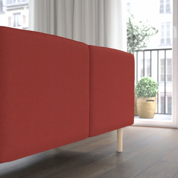 Sofá modular vermelho, encosto e almofadas de assento visíveis, colocados perto da janela com plantas.