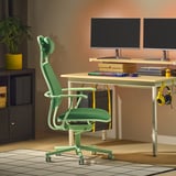 Configuração gaming moderna com cadeira LÖPARBANA verde, dois monitores, teclado e auscultadores. A cadeira é maior, com encosto alto e apoio para a cabeça.