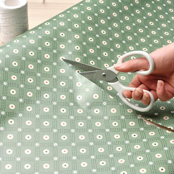 Pessoa cortando papel de embrulho floral com tesoura.