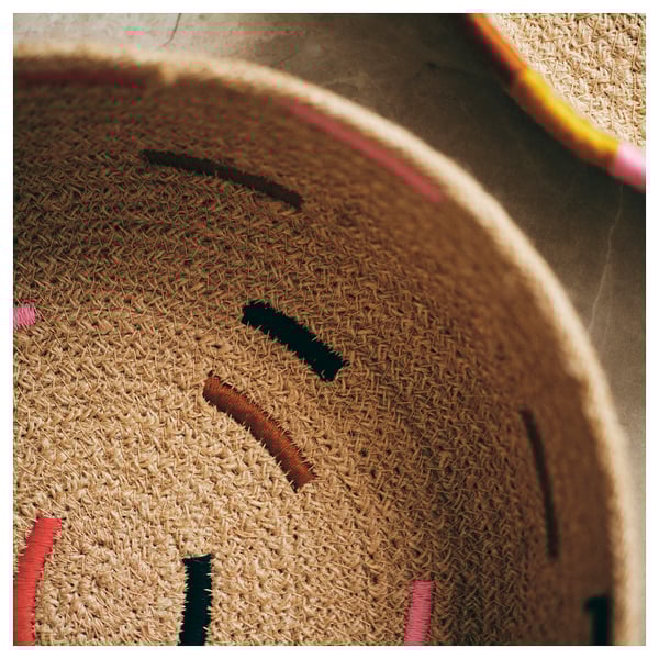 Cesta de juta natural bordada à mão, marrom com detalhes em rosa e preto. Design circular e rústico.