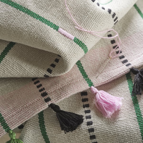 Caminho de mesa decorativo de algodão com listras verdes, detalhes em rosa e borlas amarradas à mão exibindo artesanato intrincado.