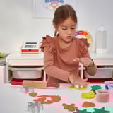 Uma jovem brinca com massa de modelar MÅLA, cortando formas com cortadores incluídos, usando um rolo de massa.