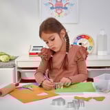 Uma garota está fazendo artesanato com papel colorido, tesoura e cortadores de biscoitos, aprimorando as habilidades motoras finas e a criatividade.