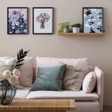 Sala de estar com sofá branco, travesseiros rosa, plantas verdes e estampas de arte de flores.