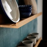 Prateleiras de madeira segurando uma tigela azul e pratos brancos; Arrumação minimalista na cozinha.