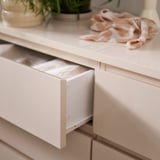 Gaveteiro moderno em madeira clara com gaveta superior aberta, decorado com plantas e lenço.