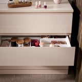 Uma cômoda MALM laranja clara aberta com um organizador de gavetas contendo itens de maquiagem como batons, pincéis e potes.