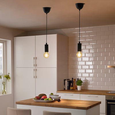 Cozinha moderna com armários brancos, balcão de madeira e duas luzes pendentes pretas iluminando uma tigela de frutas.
