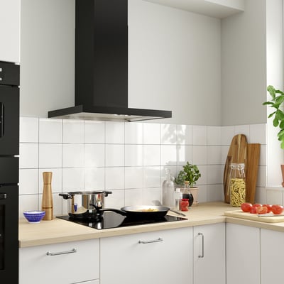 Cozinha moderna com exaustor preto, luzes led, azulejos brancos, bancada de madeira, utensílios e plantas.